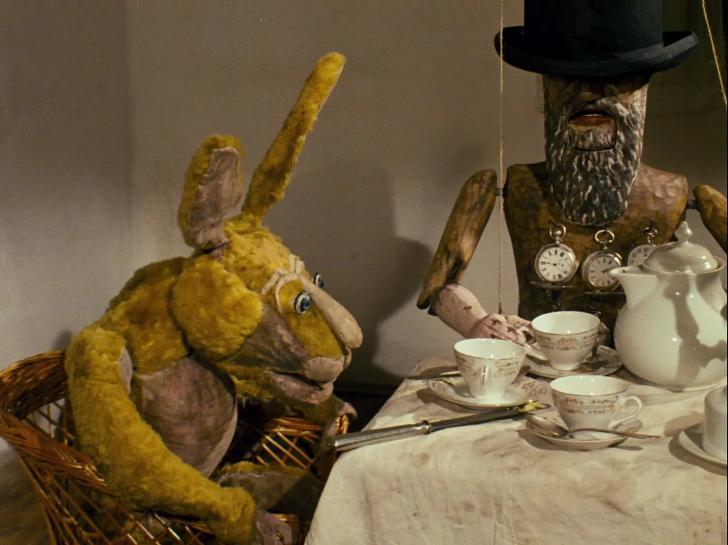 Fotograma de «Alice» de Jan Švankmajer: la Liebre de Marzo y el inquietante Sombrerero de madera en la merienda de té