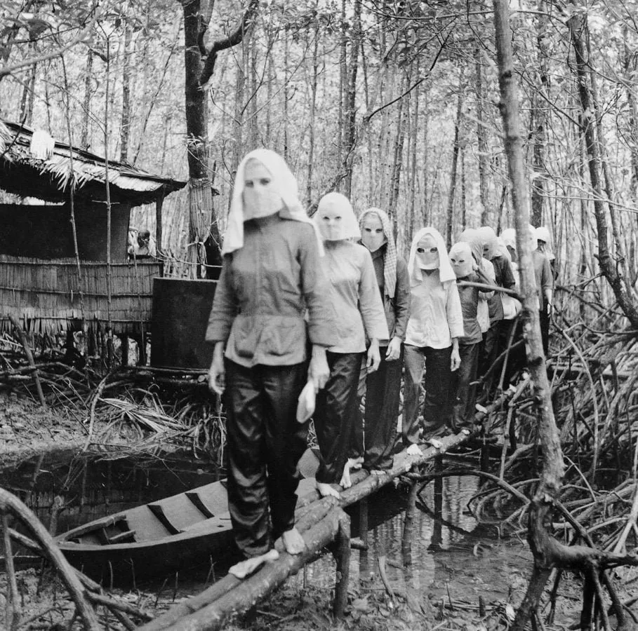 Activistas enmascaradas cruzan un puente de troncos en el delta del Mekong, fotografía de Vo Anh Khanh (1972)