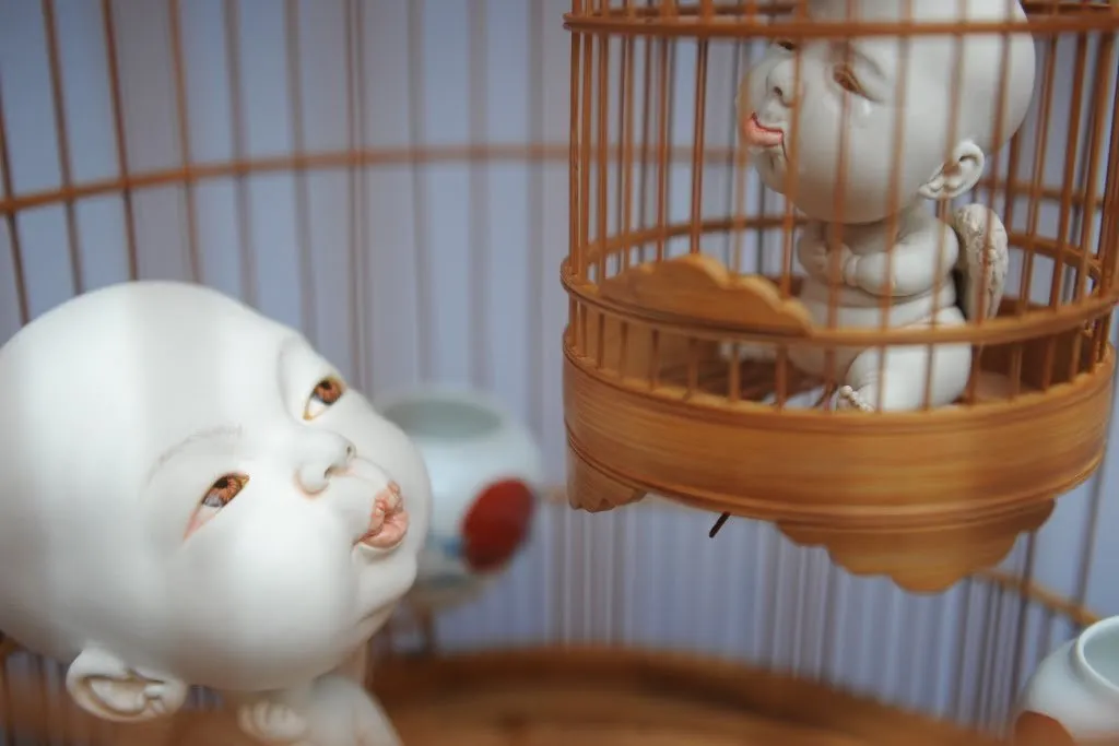 Escultura «Cages» de Johnson Tsang, con bebés de porcelana y una jaula