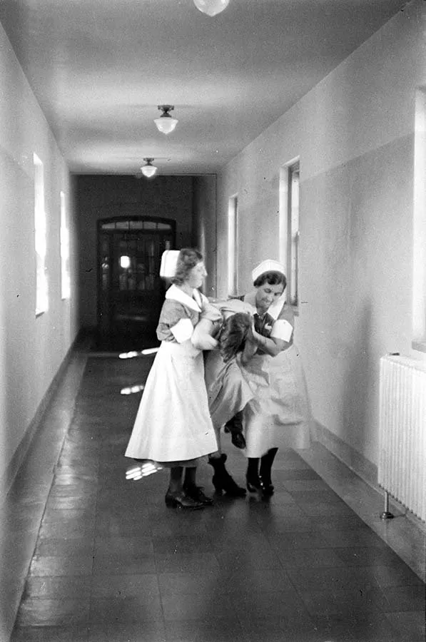 Dos enfermeras trasladan a una paciente por un pasillo del Hospital Pilgrim State (Alfred Eisenstaedt, 1938)