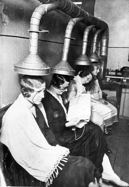 Clientas de un salón de belleza bajo secadores de casco colgantes